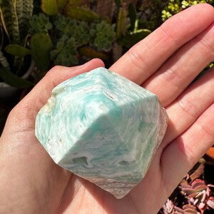 May include: A green and white, faceted, polished,  crystal gemstone. The crystal is shaped like a pyramid with a rounded top.