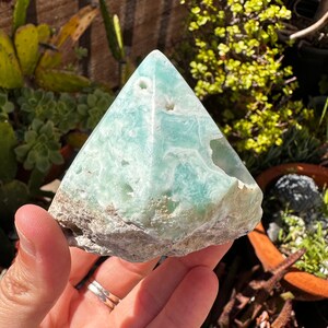 May include: A light green, naturally formed, crystal pyramid with a rough, textured surface.