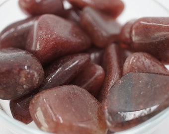 May include: A collection of tumbled red jasper stones in a clear glass bowl. The stones are smooth and polished, with a deep red color.