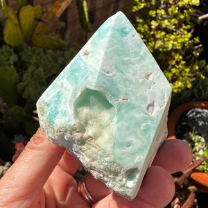 May include: A light blue and white celestite crystal in the shape of a pyramid. The crystal has a natural, rough texture and is translucent.