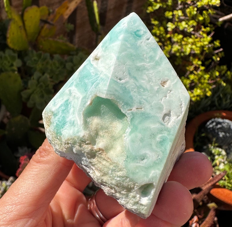 May include: A light blue and white celestite crystal in the shape of a pyramid. The crystal has a natural, rough texture and is translucent.