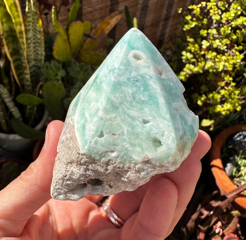 May include: A light green celestite crystal with a rough, natural texture. The crystal is shaped like a pyramid and has a white, cloudy appearance.
