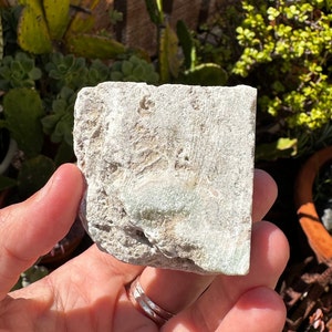 May include: A rough, white, and green stone with a natural, irregular shape. The stone has a light green hue and a rough, textured surface.