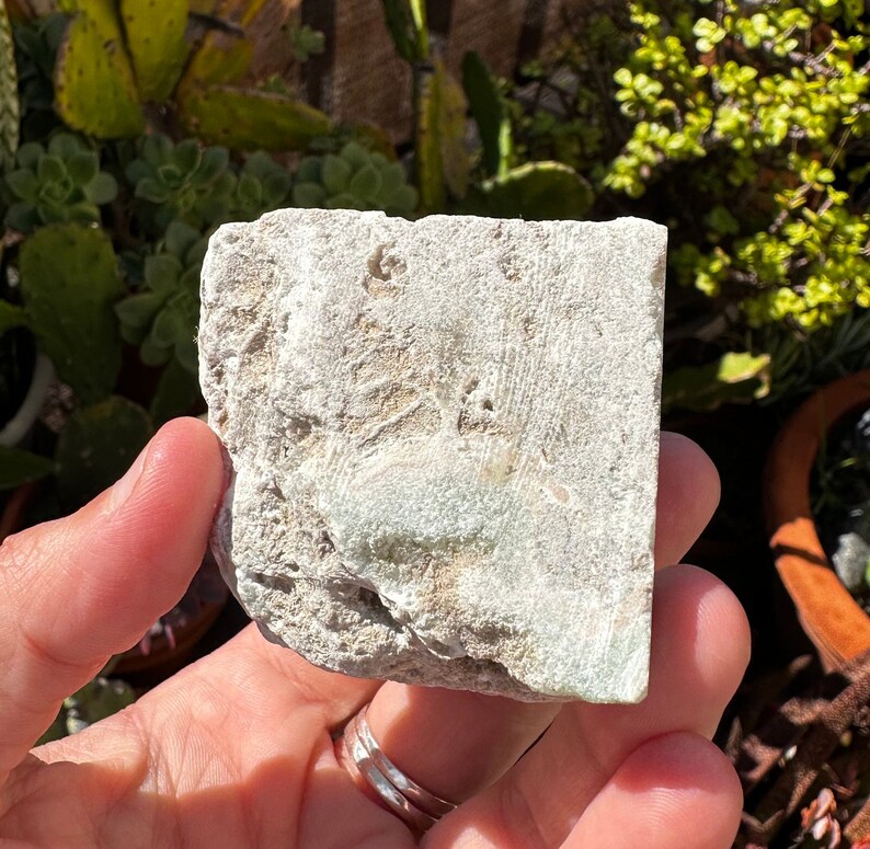 May include: A rough, white, and green stone with a natural, irregular shape. The stone has a light green hue and a rough, textured surface.