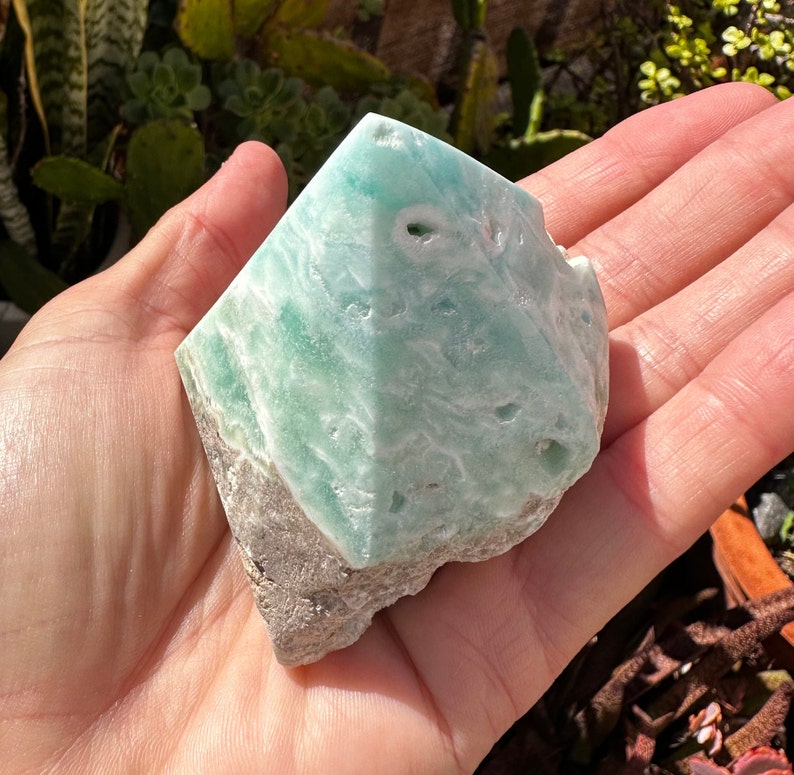 May include: A light green and white celestite crystal with a rough, natural texture. The crystal is shaped like a pyramid and has a smooth, polished surface.