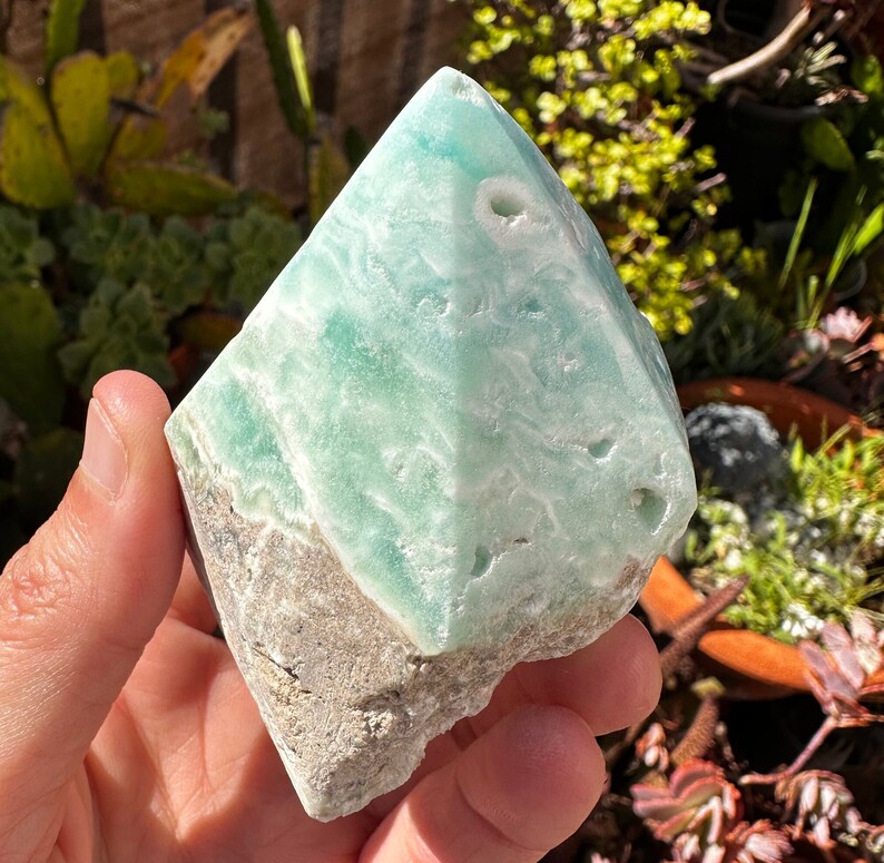 May include: A light green and white celestite crystal point with a rough, natural texture. The crystal has a unique, swirling pattern and several small holes.