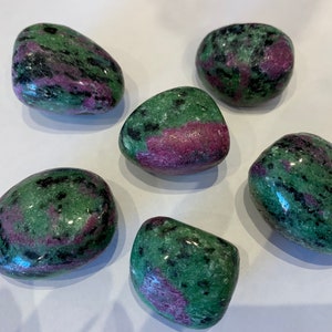 May include: Six smooth, green, pink, and black tumbled stones. The stones are polished and have a variety of patterns.