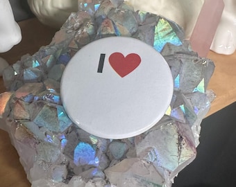 May include: A white button with the text "I love" and a red heart. The button is sitting on a cluster of iridescent crystals.