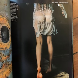 以下が含まれることがあります： 白い透き通ったドレスを着た女性の白黒写真。女性はカメラに向かって背を向けて立っており、足が見えている。画像は雑誌からで、右上に「HOW TO SEE BETTER PICTURES」というテキストが見える。