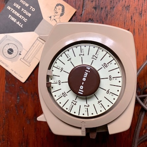 May include: A beige and brown Intermatic Time-All timer with a round dial and a cord. The dial has numbers 1 through 12, AM and PM markings, and the words "time-all". The instructions for using the timer are visible in the background.