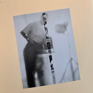 May include: A black and white photo of a person standing with their back to the camera. The photo is cut in half vertically, with the right side showing a close-up of a watch.