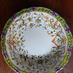 May include: A white ceramic bowl with a scalloped rim and a colorful floral design. The bowl features a blue, red, green, and yellow floral pattern.