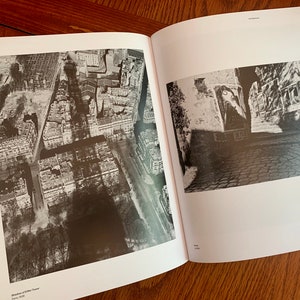 May include: Two black and white photographs of a city. The first photo is an aerial view of a city with buildings and streets. The second photo is a street view of a city with buildings and cobblestone streets.