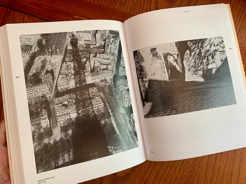 May include: Two black and white photographs of a city. The first photo is an aerial view of a city with buildings and streets. The second photo is a street view of a city with buildings and cobblestone streets.