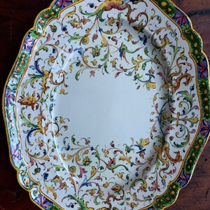 May include: A white oval ceramic serving platter with a colorful floral design. The border features a green, yellow, and blue floral pattern.
