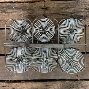 Może przedstawiać: Zestaw sześciu srebrnych szpuli do wywoływania filmu w metalowym stojaku. Szpule są zaprojektowane do przechowywania filmu fotograficznego w celu przetworzenia.