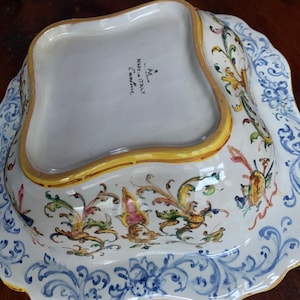May include: A white ceramic serving dish with a blue and yellow floral design. The bottom of the dish is marked "Made in Italy,  *A*L,  Ceramica".