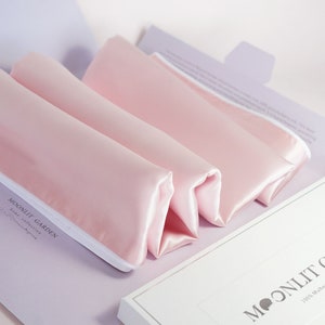 May include: Three pink silk pillowcases folded inside a white box with the text "MOONLIT GARDEN 100% Mulberry Silk Pillowcases" printed on the front.