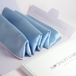 May include: A set of three light blue silk sleep masks folded and packaged in a white box with the text "MOONLIT GARDEN 100% Mulberry Silk Pajamas".