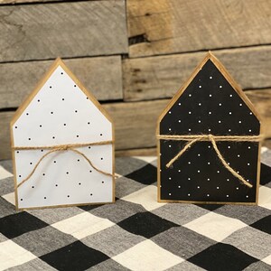 May include: Two wooden house-shaped decorations with black and white polka dot patterns. The houses are tied with twine and are sitting on a black and white checkered surface.