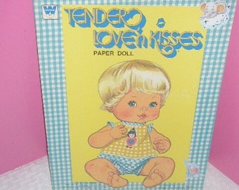 May include: Vintage "Tender Love n Kisses" paper doll box. The box features a baby doll illustration on a yellow background, wearing a yellow and blue outfit. The box has a blue and white checkered border.