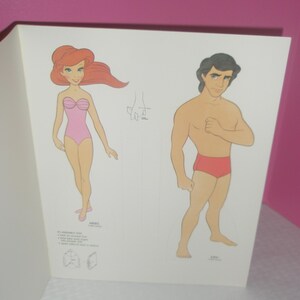 Puede incluir: Una hoja de papel con dos personajes ilustrados, Ariel y Eric, dise&ntilde;ados como figuras para recortar. Ariel tiene el pelo largo y rojo y un ba&ntilde;ador rosa, mientras que Eric tiene el pelo oscuro y un ba&ntilde;ador rojo. Incluye instrucciones de montaje.