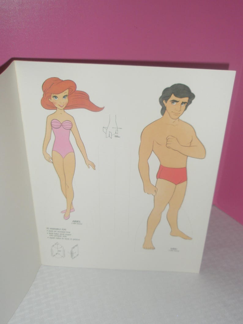 Puede incluir: Una hoja de papel con dos personajes ilustrados, Ariel y Eric, dise&ntilde;ados como figuras para recortar. Ariel tiene el pelo largo y rojo y un ba&ntilde;ador rosa, mientras que Eric tiene el pelo oscuro y un ba&ntilde;ador rojo. Incluye instrucciones de montaje.