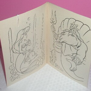 May include: A coloring book open to two pages, featuring line art illustrations. One page shows a mermaid with a fish, the other shows a bearded man on a throne. The images are in black and white.