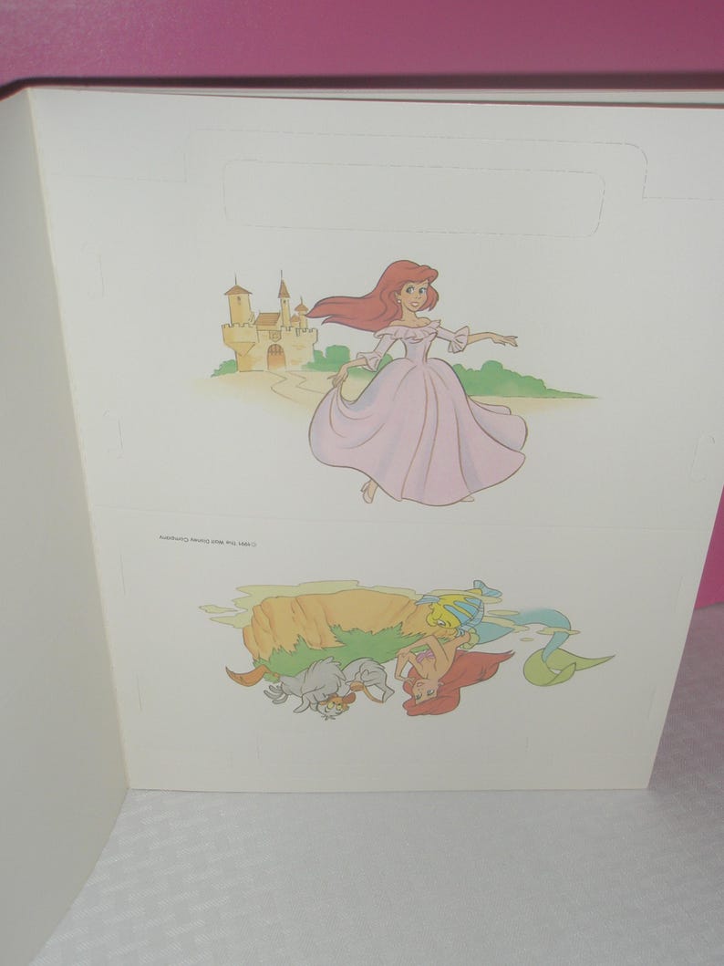 Puede incluir: Una hoja de papel blanca con dos ilustraciones de un personaje pelirrojo. La imagen superior muestra al personaje con un vestido morado claro cerca de un castillo. La imagen inferior invertida muestra al personaje como sirena con pez y cangrejo.