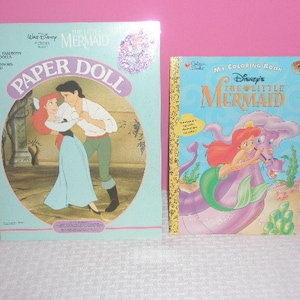 May include: Two vintage Disney's The Little Mermaid items. A paper doll set with Ariel and Prince Eric, and a coloring book featuring Ariel and her friends. Both items have colorful illustrations and text.