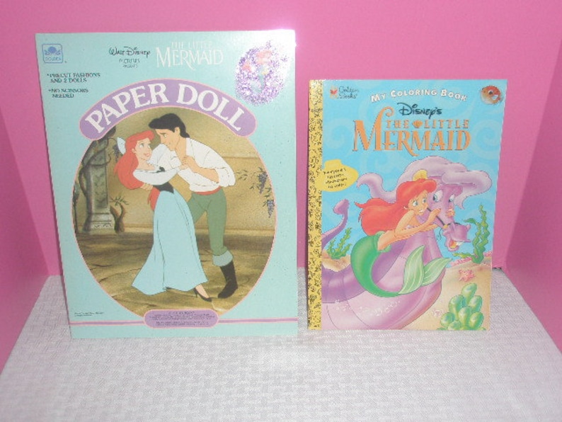 May include: Two vintage Disney's The Little Mermaid items. A paper doll set with Ariel and Prince Eric, and a coloring book featuring Ariel and her friends. Both items have colorful illustrations and text.