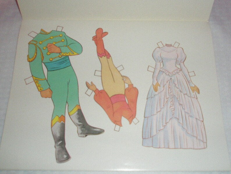 May include: Paper doll set featuring a green and gold uniform, a pair of orange pants and top, and a white wedding dress. The illustrations are outlined in brown and have tabs for cutting out the figures.