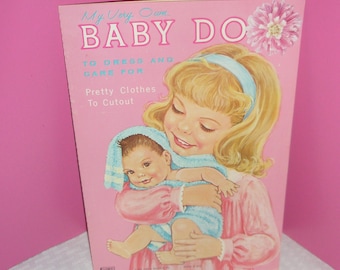 Könnte beinhalten: Ein Vintage-Kinderbuch in Rosa und Weiß mit dem Titel "My Very Own Baby Doll". Das Cover zeigt eine blonde Mädchen, das eine Babypuppe hält. Der Text auf dem Buch lautet "To Dress and Care For" und "Pretty Clothes To Cutout".