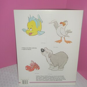 Puede incluir: Una contraportada rectangular blanca de un libro de mu&ntilde;ecas de papel con ilustraciones coloridas de un pez amarillo, una gaviota blanca, un cangrejo rojo y un perro gris. El texto incluye Press out play pieces, Fold to stand y una descripci&oacute;n.