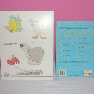 May include: Two children's books are displayed. One features illustrations of cartoon characters, including a yellow fish, a white seagull, a gray dog, and a red crab. The other book has a blue cover with gold trim and text.