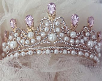 May include: A gold crown with pink gemstones and white pearls. The crown is decorated with intricate details and is a beautiful accessory for any occasion.