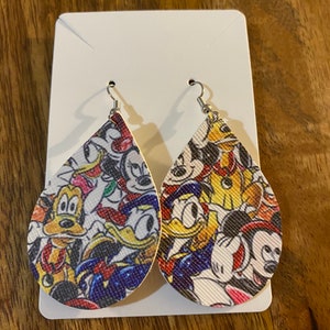 May include: Teardrop-shaped earrings featuring a colorful pattern of cartoon characters, including Mickey Mouse, Donald Duck, and Goofy. The earrings are attached to silver-colored fish hook ear wires and are displayed on a white card.