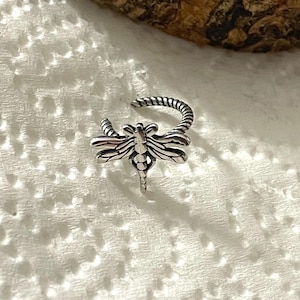May include: Silver ring featuring a dragonfly design. The ring is twisted and has a delicate, detailed dragonfly design.
