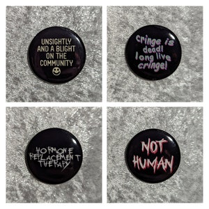 May include: Four black button pins with white and pink text. The pins say "Unsightly and a blight on the community", "Cringe is dead! Long live cringe!", "Hormone replacement therapy", and "Not human".