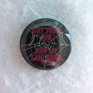 May include: A round, black button with a white spiderweb design and red text that reads "QUIT YOUR JOB JOIN MY EMO BAND."