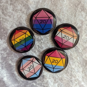 May include: Five 20-sided dice with different pride flag designs. The dice are black with white outlines and the number 20 in white.