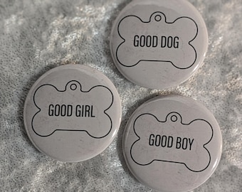 May include: Three round, light gray dog tags with black text and a bone-shaped design. The tags read "GOOD DOG", "GOOD GIRL", and "GOOD BOY". Each tag has a small hole at the top for attachment to a collar.