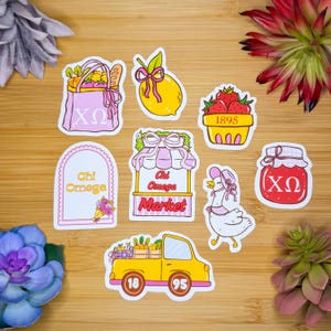 May include: A collection of colorful stickers featuring various designs. Includes a pink tote bag with Greek letters, a yellow lemon, a basket of strawberries, a Chi Omega Market stand, a duck, a jar of jam, and a yellow truck.