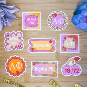 Könnte beinhalten: Ein Set mit neun Aufklebern mit den griechischen Buchstaben Alpha Phi in verschiedenen Designs. Die Aufkleber sind rosa, orange und gelb mit verschiedenen Mustern und Grafiken, darunter Blumen, Sterne und eine Kirsche.
