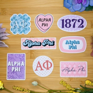 Könnte beinhalten: Ein Set mit neun Aufklebern mit verschiedenen Designs im Zusammenhang mit der Alpha Phi Sorority. Die Aufkleber sind in Pink, Blau und Lila mit Blumenmustern und den Buchstaben "AΦ" sowie den Worten "Alpha Phi".
