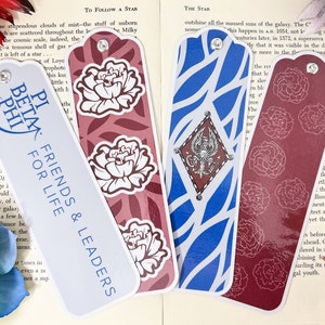 May include: Four colorful bookmarks with different designs. One bookmark is white with blue text that reads "Pi Beta Phi. Friends & Leaders for Life". Another bookmark is red with white floral designs. A third bookmark is blue with white stripes and a white crest with a bird design. The final bookmark is red with white floral designs.