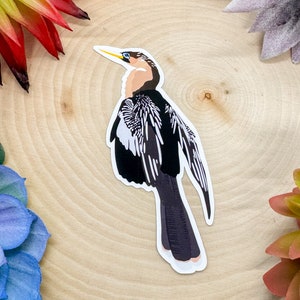Peut inclure: Un autocollant d'oiseau noir et blanc avec un long cou et un bec jaune. L'oiseau est debout sur une surface en bois.