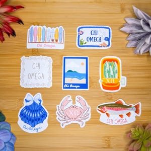 May include: A set of nine stickers featuring various beach-themed designs. The stickers include a seashell, a crab, a fish, a beach scene, a surfboard rack, a fish market, and three different designs with the text "Chi Omega".