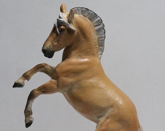 May include: A tan-coloured horse figurine rearing up on its hind legs. The horse has a light-coloured mane and tail. The figurine is detailed and appears to be made of a ceramic or resin material. The horse is a decorative item.