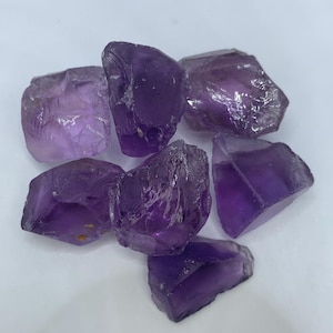 Puede incluir: Un conjunto de seis piedras de amatista en bruto con tonos morados profundos y estructuras cristalinas translúcidas y dentadas. Cada pieza muestra facetas naturales y formas irregulares con distintos niveles de claridad y textura de cuarzo.